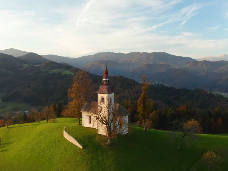 Crkva na brežuljku u Sloveniji okružena prirodom i planinama, idealna za miran odmor i šetnju.